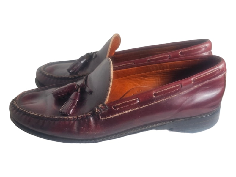 May include: A pair of burgundy leather tassel loafers with a brown leather sole. The loafers have a classic design and are perfect for casual or semi-formal occasions.