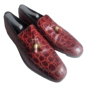 May include: A pair of burgundy leather loafers with a crocodile pattern and gold tassels.