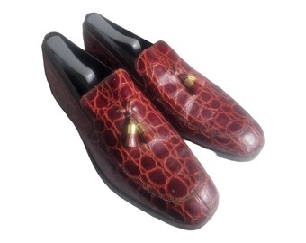 Pode incluir: Um par de sapatos de couro bordô com padrão de crocodilo e borlas douradas.