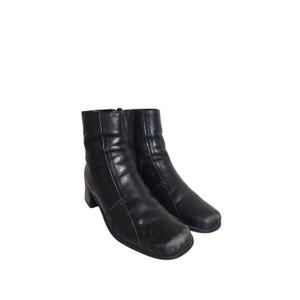 May include: A pair of black ankle boots featuring a square toe, a block heel, and a side zipper closure. The boots have visible vertical seam detailing running along the front and sides, with a smooth finish and slight wear on the toe area.