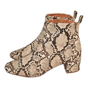 May include: A pair of ankle boots with a snakeskin pattern in shades of brown and white. The boots have a block heel and a pointed toe.