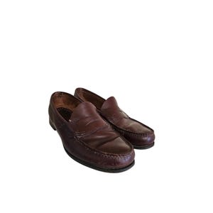 May include: A pair of dark brown leather penny loafers. The shoes have a classic design with a rounded toe and a strap across the vamp. The leather appears worn, with visible creases and a slightly faded color.