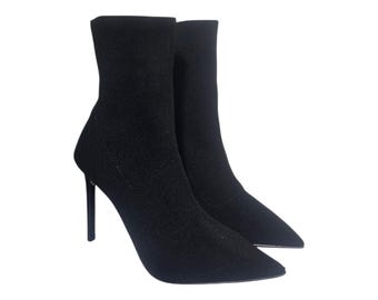 May include: A pair of black ankle boots with stiletto heels. The boots have a pointed toe and a textured fabric upper. The heels are approximately 4 inches (10 cm) high. The boots are set against a white background.