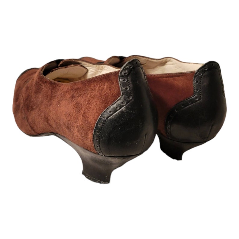 May include: A pair of brown suede heeled shoes with black leather accents. The shoes have a pointed toe and a small heel.