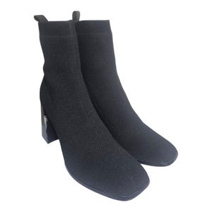 May include: A pair of black ankle boots with a sock-like upper and a square toe. The boots have a block heel, approximately 7.6 cm high. The boots are made of a knit material.
