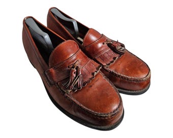 May include: A pair of brown leather tassel loafers. The loafers have a fringe detail and a pointed toe.