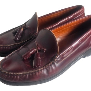 May include: A pair of burgundy leather tassel loafers with a brown leather sole. The loafers have a classic design and are perfect for casual or semi-formal occasions.