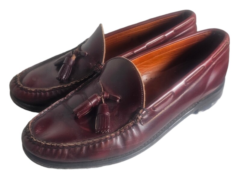 May include: A pair of burgundy leather tassel loafers with a brown leather sole. The loafers have a classic design and are perfect for casual or semi-formal occasions.