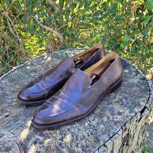 Pode incluir: Um par de sapatos marrons de couro com um visual ligeiramente desgastado. Os sapatos t&ecirc;m uma ponta pontiaguda e um salto baixo.