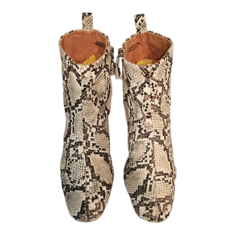 May include: A pair of ankle boots with a snake print pattern. The boots are made of a light brown leather with black markings. The boots have a zipper on the inside of each boot.