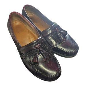 May include: A pair of dark brown leather loafers with tassel details. The shoes have a classic design with a rounded toe and a stitched sole. The interior lining is a lighter brown color.