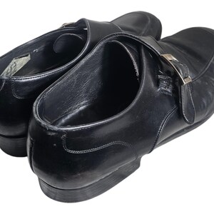 Pode incluir: Um par de sapatos de couro preto com fecho de fivela. Os sapatos t&ecirc;m bico fino e salto baixo.