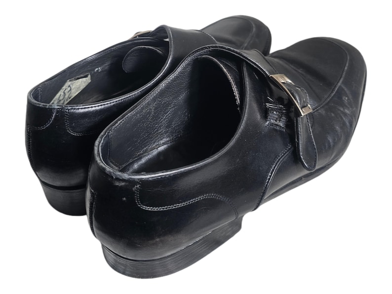 Pode incluir: Um par de sapatos de couro preto com fecho de fivela. Os sapatos t&ecirc;m bico fino e salto baixo.