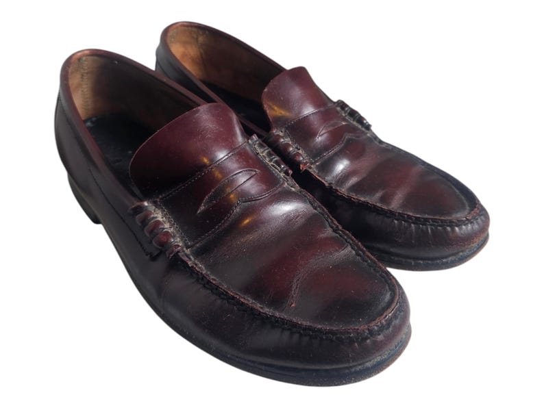 May include: A pair of dark brown leather loafers with a penny strap detail. The loafers have a slightly worn look and are made of a high-quality leather.