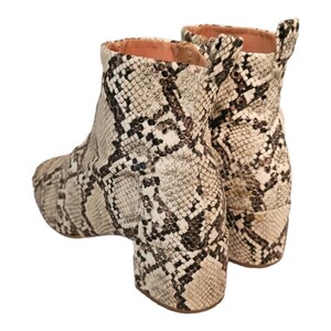 May include: A pair of ankle boots with a snakeskin pattern. The boots are a light brown color with black markings. The boots have a block heel.