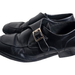 Pode incluir: Sapatos de monge de couro preto com fivela prateada.