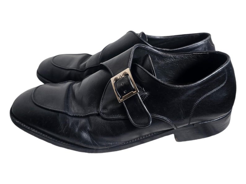 Pode incluir: Sapatos de monge de couro preto com fivela prateada.