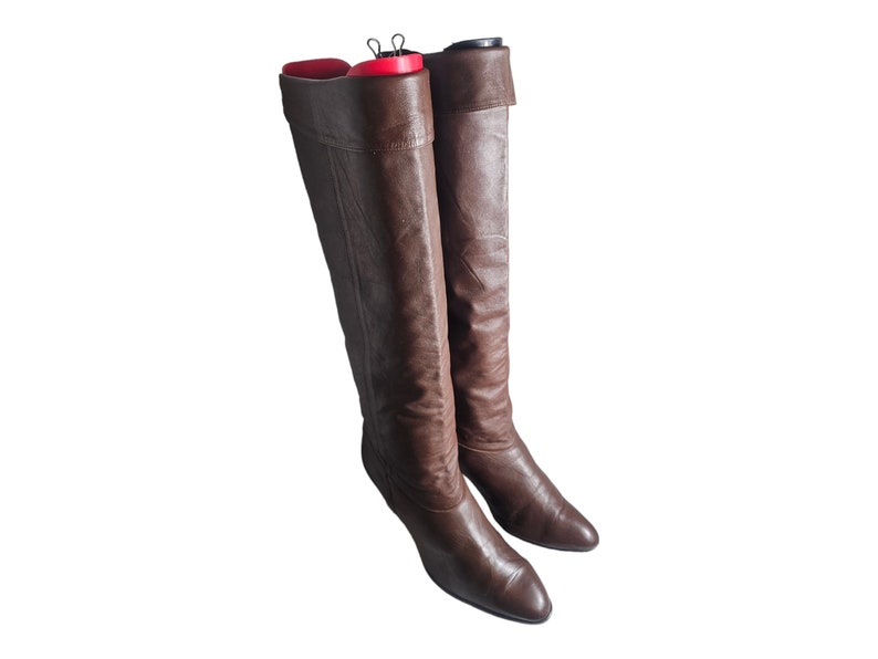 May include: A pair of brown leather knee-high boots with a pointed toe.