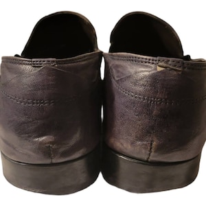 May include: A pair of dark purple leather loafers with a slightly worn look. The shoes have a rounded toe and a low heel.