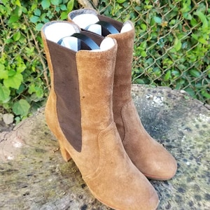 May include: A pair of brown suede ankle boots with a block heel. The boots have a brown elastic panel on the back and a pointed toe.