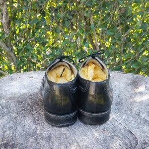 Puede incluir: Un par de zapatos de cuero negro con cordones, llenos de patatas fritas amarillas, sentados en un toc&oacute;n de &aacute;rbol.
