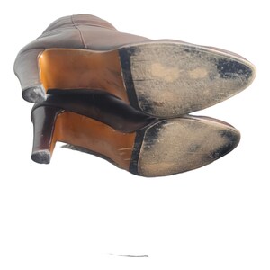May include: A pair of brown leather heeled boots with worn soles. The boots are stacked on top of each other.