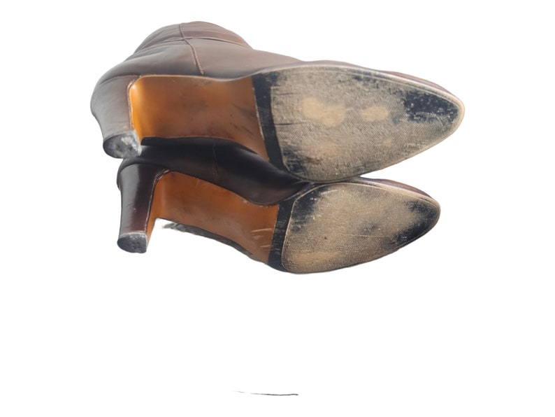 May include: A pair of brown leather heeled boots with worn soles. The boots are stacked on top of each other.