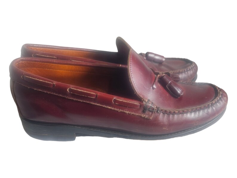 May include: A pair of burgundy leather tassel loafers with a brown leather sole.