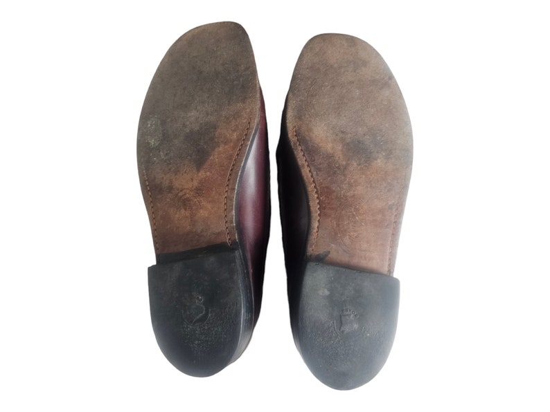 May include: A pair of brown leather loafers with black soles. The soles have a textured pattern and the shoes are worn.