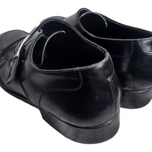 Pode incluir: Um par de sapatos de couro preto com fecho de fivela. Os sapatos t&ecirc;m bico fino e salto baixo.