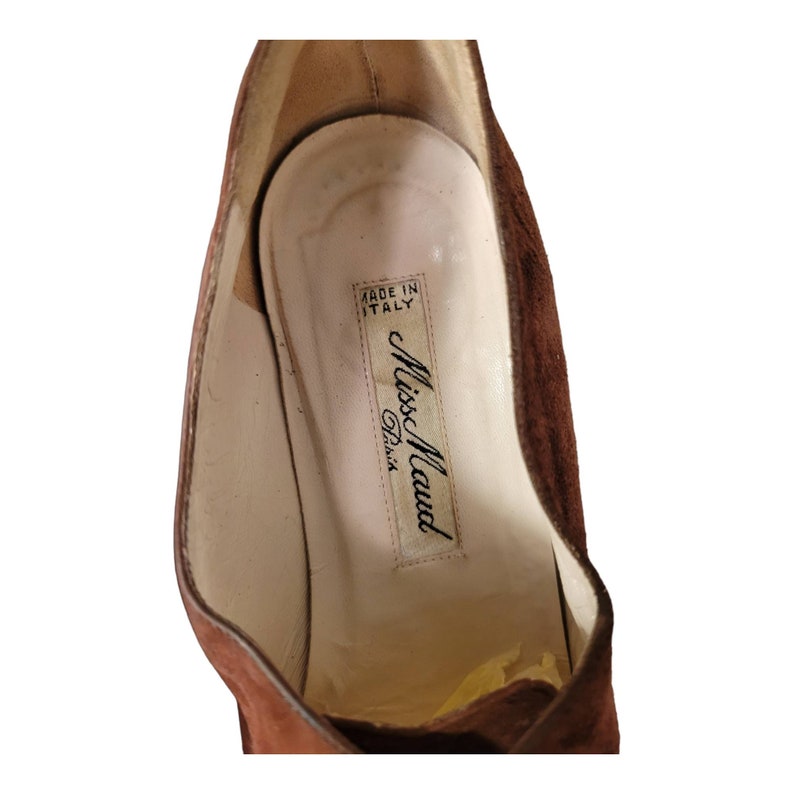 May include: Close-up of the inside of a brown suede shoe with a white label that reads "Made in Italy" and "Miss Maud Paris".