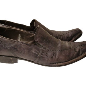 May include: A pair of brown leather slip-on shoes with pointed toes and decorative stitching. The shoes have a low heel and a slightly pointed toe.