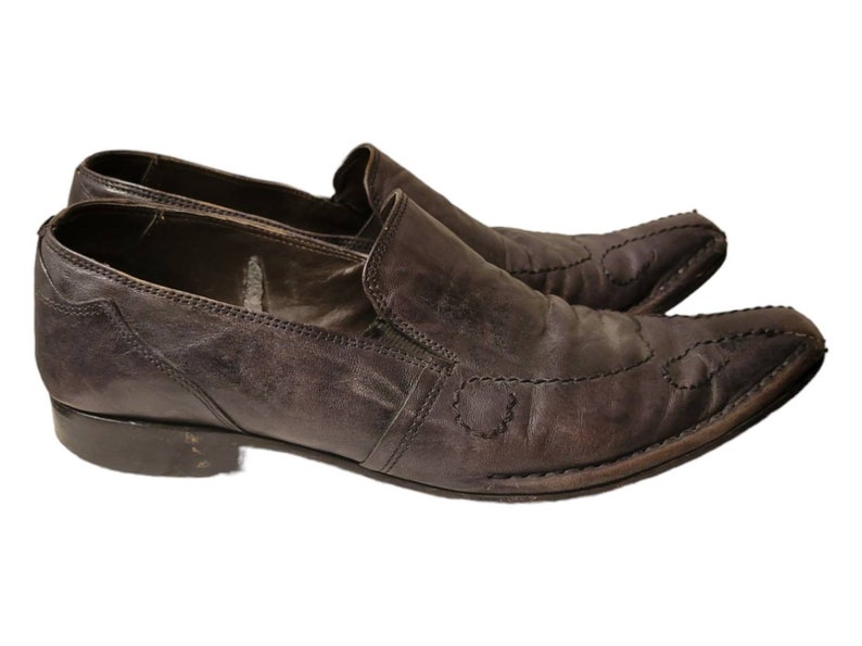 May include: A pair of brown leather slip-on shoes with pointed toes and decorative stitching. The shoes have a low heel and a slightly pointed toe.