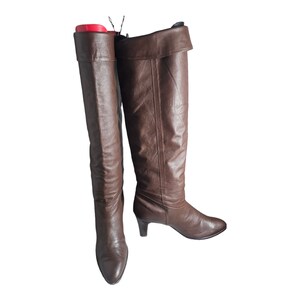 May include: A pair of brown leather knee-high boots with a slight heel. The boots have a fold-over top and a pointed toe.