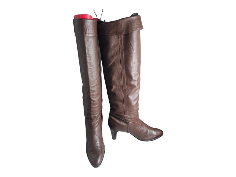 May include: A pair of brown leather knee-high boots with a slight heel. The boots have a fold-over top and a pointed toe.