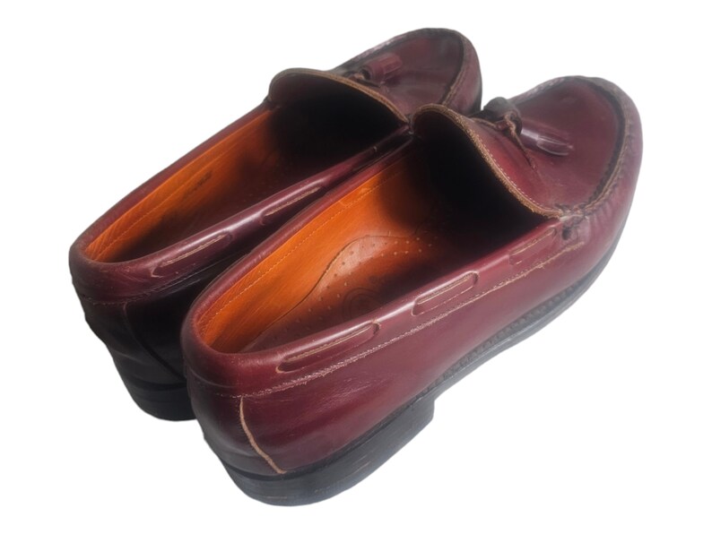 May include: A pair of burgundy leather loafers with tassels. The loafers have a classic design and are made of high-quality leather.