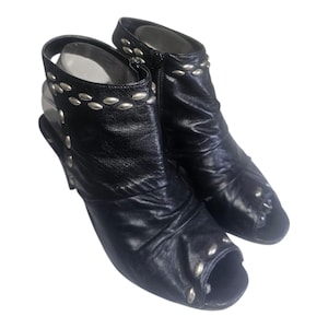 Könnte beinhalten: Ein Paar schwarze Leder-Peep-Toe-Slingback-Stiefel. Die Stiefel haben silberfarbene Nietenbesätze an Oberseite und Seiten. Die Absätze sind im Stiletto-Stil.