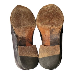 May include: A pair of brown leather dress shoes with black soles. The shoes are worn and have scuff marks on the soles.