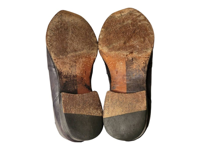 May include: A pair of brown leather dress shoes with black soles. The shoes are worn and have scuff marks on the soles.