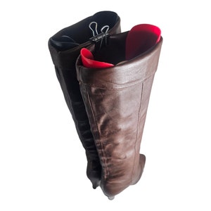 May include: A pair of brown leather boots with a pointed toe, held together with a metal clip. The boots are folded down at the top, revealing a red lining.
