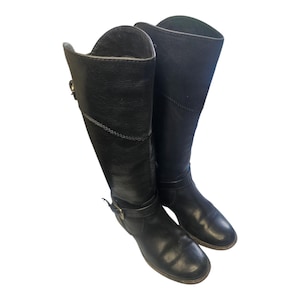 May include: A pair of black leather knee-high boots. The boots have a rounded toe, a buckle detail on the side, and a folded-over top. The boots are made of a smooth, shiny leather material.