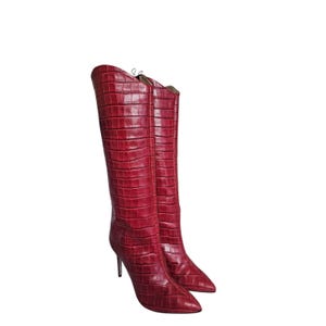 May include: A pair of knee-high boots in a deep red color featuring a textured crocodile-embossed pattern. These boots have a pointed toe design, a tall shaft that reaches the knee, and a slim stiletto heel, providing a sleek and structured look.