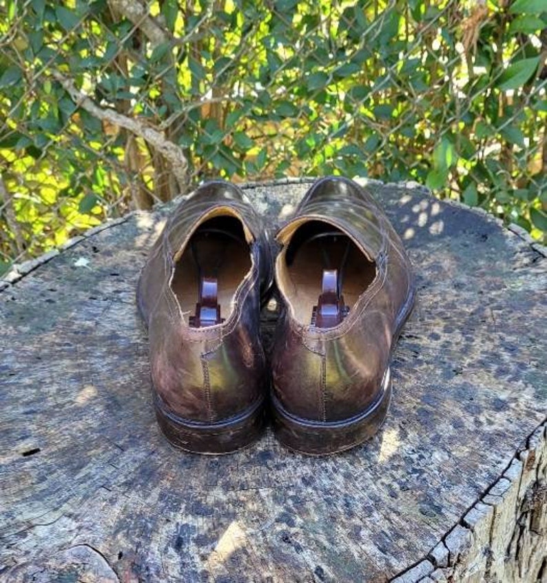 Pode incluir: Um par de sapatos de couro marrom com bico fino e design de deslizamento. Os sapatos t&ecirc;m um forro de couro marrom e uma sola de borracha.