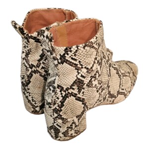 May include: A pair of ankle boots with a snakeskin pattern in shades of brown and white. The boots have a block heel and a pointed toe.