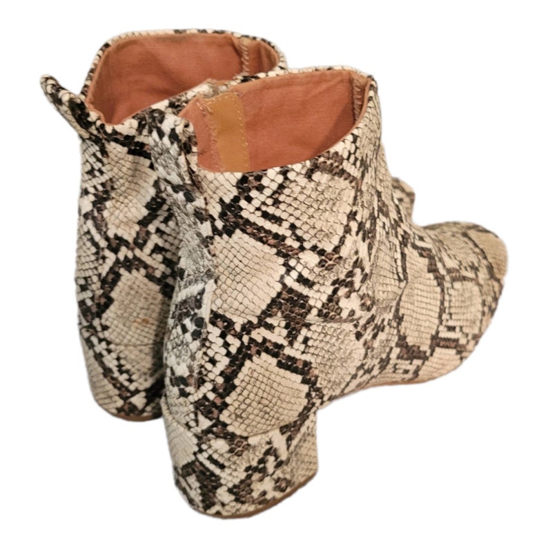 May include: A pair of ankle boots with a snakeskin pattern in shades of brown and white. The boots have a block heel and a pointed toe.