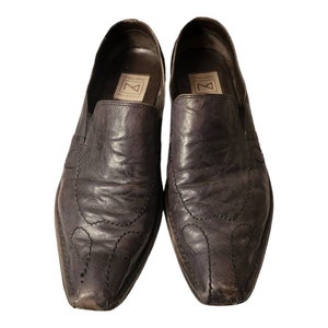 May include: A pair of dark brown leather slip-on shoes with a pointed toe and decorative stitching. The shoes have a leather insole and a rubber outsole.