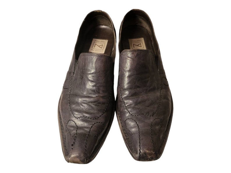 May include: A pair of dark brown leather slip-on shoes with a pointed toe and decorative stitching. The shoes have a leather insole and a rubber outsole.