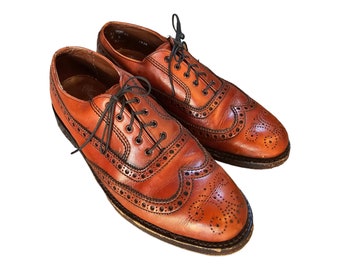 May include: A pair of brown leather brogue shoes with black laces. The shoes have a wingtip design and are made of smooth leather.