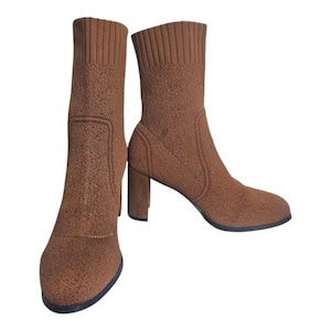 May include: A pair of brown ankle boots made from a textured knit fabric. The boots feature a rounded toe, a block heel, and a ribbed knit upper that reaches the ankle. The heels are approximately 7.6 cm high.