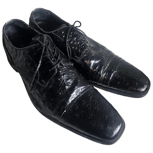 May include: A pair of black leather dress shoes with an ostrich skin pattern. The shoes have a lace-up closure and a pointed toe.